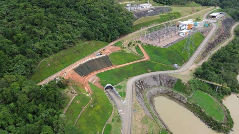 Aerial view of a landfill or waste management facility with earthen berms, access roads, and processing areas surrounded by green vegetation