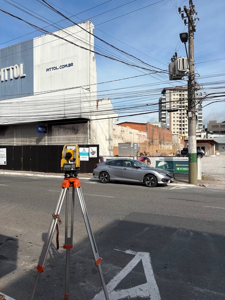 A surveying instrument on tripod positioned in a street with buildings and a parked car in the background